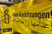 Amnesty Infostand mit einem Banner auf dem "Stoppt Hinrichtungen" auf deutsch und arabisch geschrieben steht. Daneben ein Aufsteller mit dem Amnesty-Logo.